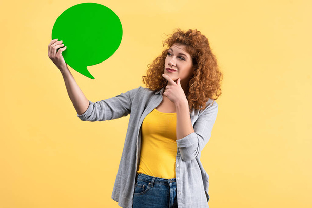 pensive woman looking at empty green speech bubble, isolated on yellow   - Fotoğraf, Görsel