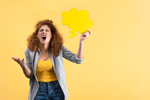 angry woman yelling and holding empty speech bubble in shape of cloud, isolated on yellow  - Photo, Image