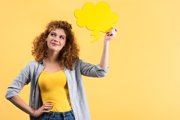 pensive smiling woman holding empty speech bubble in shape of cloud, isolated on yellow  - Photo, Image