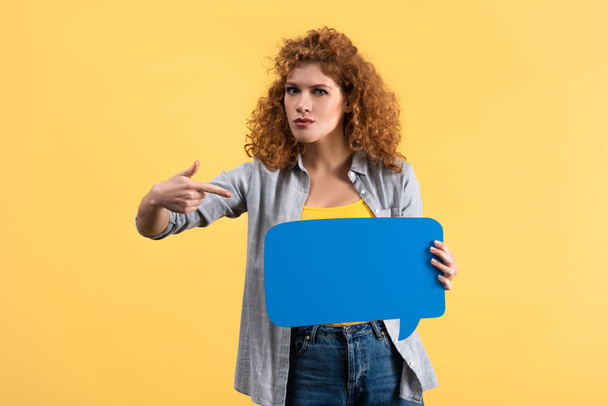 serious woman pointing at empty speech bubble, isolated on yellow  - Foto, afbeelding