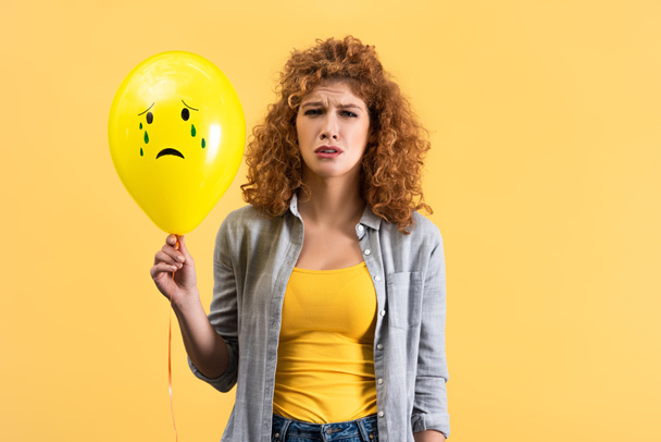 boos roodharige meisje met droevige ballon met tranen, geïsoleerd op geel - Foto, afbeelding