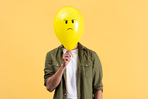 young man holding angry balloon in front of face, isolated on yellow - Fotoğraf, Görsel