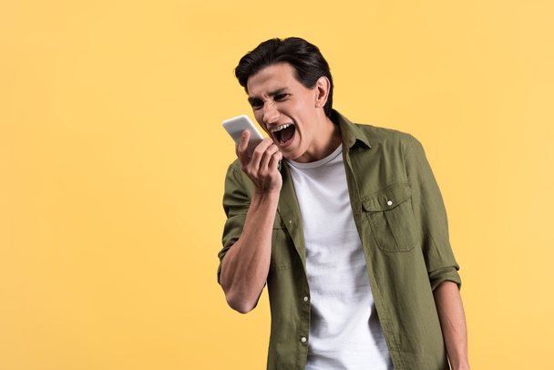 angry young man screaming at smartphone, isolated on yellow - Photo, Image