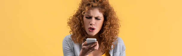 Akıllı telefondan bağıran, sarıda izole edilmiş kızgın kızıl saçlı kadının panoramik görüntüsü - Fotoğraf, Görsel
