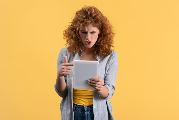 aggressive girl pointing and shouting at digital tablet, isolated on yellow - Foto, immagini