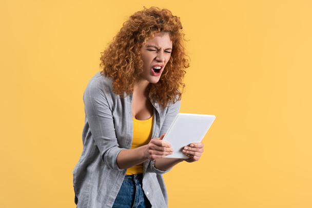 angry redhead girl shouting at digital tablet, isolated on yellow - Φωτογραφία, εικόνα
