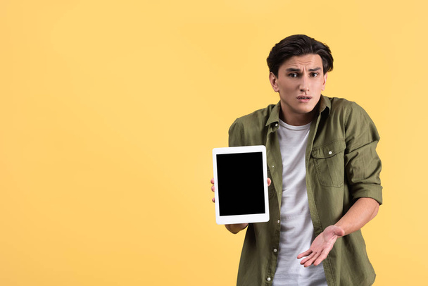 confused man showing digital tablet with blank screen, isolated on yellow - Foto, imagen