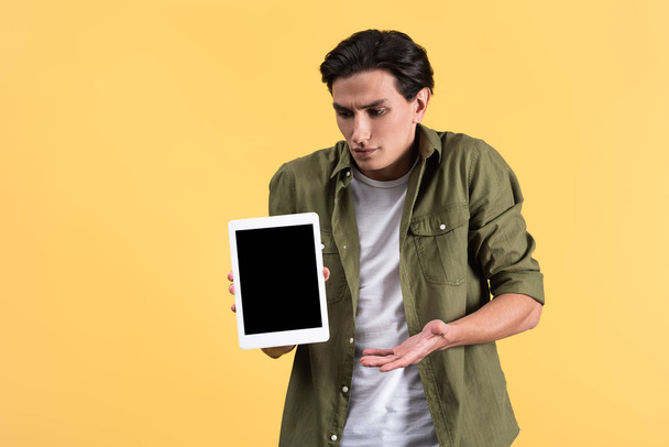 Boş ekranlı dijital tablet gösteren hayal kırıklığına uğramış bir adam, sarı ekranda izole edilmiş. - Fotoğraf, Görsel