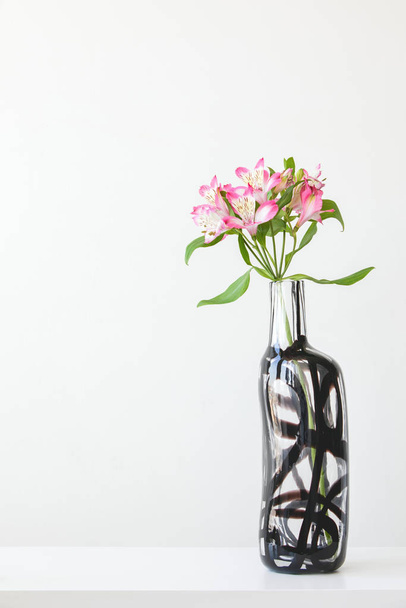 Różowa alstroemeria w szklanym wazonie na białym stole - Zdjęcie, obraz