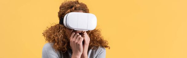 panoramic shot of scared redhead woman using vr headset, isolated on yellow - Foto, afbeelding