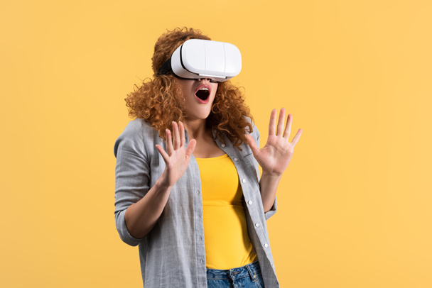 shocked redhead woman using virtual reality headset, isolated on yellow - Foto, afbeelding