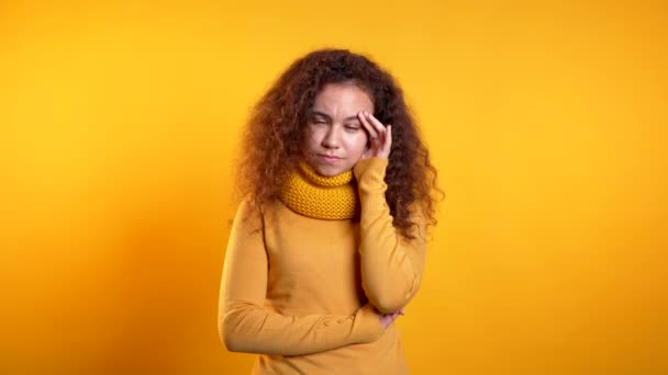Young beautiful upset woman with curly hair on yellow studio portrait. Girl putting hands on head. Concept of problems - 映像、動画
