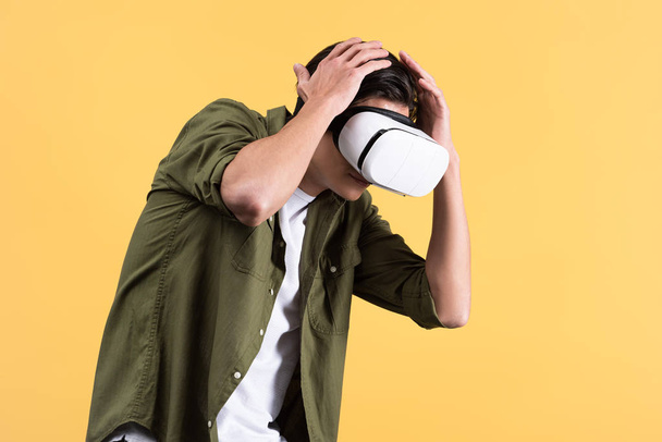 frightened young man using virtual reality headset, isolated on yellow - Photo, Image