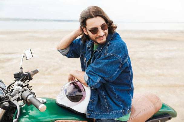 Positive optimistic happy man biker on his bike outdoors on a beach. - Фото, изображение