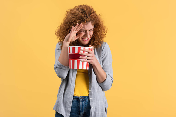 scared girl watching movie with bucket of popcorn, isolated on yellow  - Photo, image