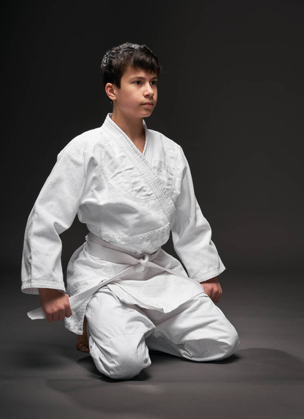 sport concept - a teenager dressed in martial arts clothing poses on a dark gray background, studio shoot - Photo, Image