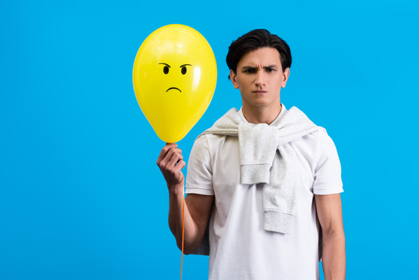 jovem irritado segurando balão amarelo, isolado em azul
 - Foto, Imagem