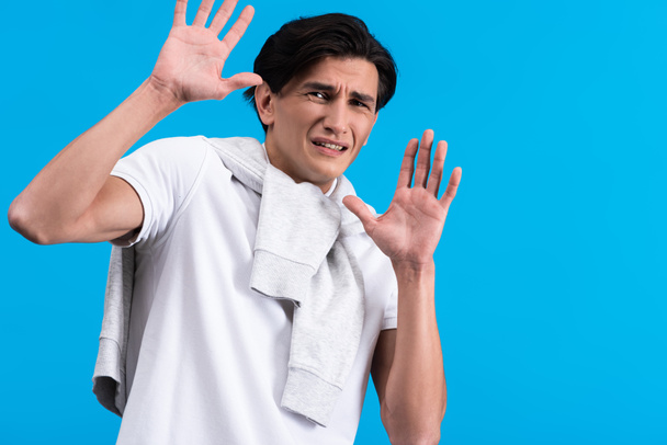 portrait of frightened young man with hands up, isolated on blue - Fotoğraf, Görsel