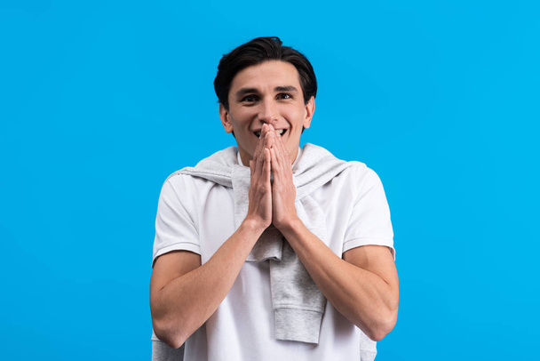 portrait of surprised young man holding hands together, isolated on blue - Foto, imagen