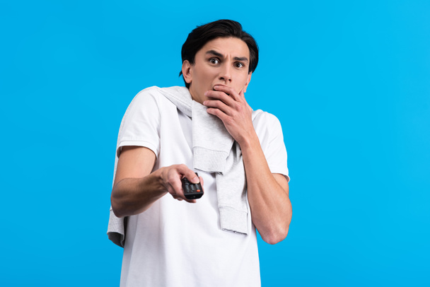 shocked man watching tv with remote controller, isolated on blue - Foto, immagini