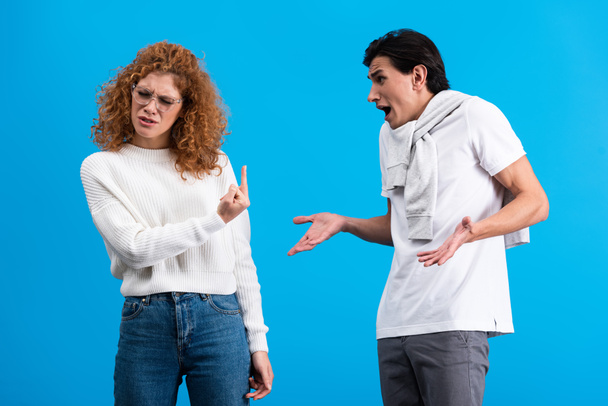 irritated girlfriend showing middle finger to angry boyfriend, isolated on blue - Фото, изображение
