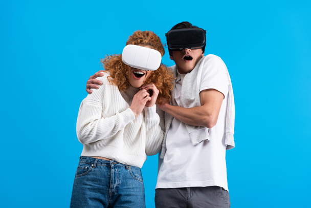 surprised couple using virtual reality headsets, isolated on blue - Photo, Image