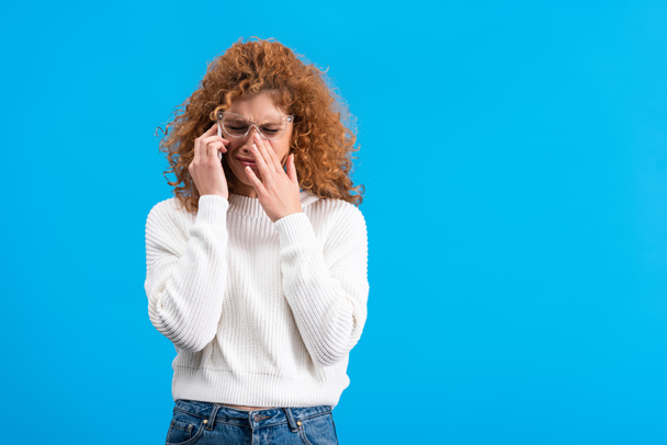плаче руда жінка в окулярах розмовляє на смартфоні, ізольована на синьому
 - Фото, зображення