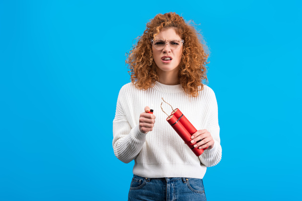 irritated woman in eyeglasses holding dynamite and lighter, isolated on blue - Fotoğraf, Görsel