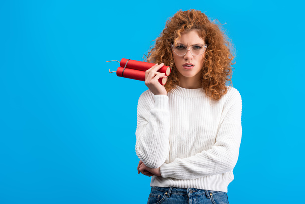confused woman in eyeglasses holding dynamite, isolated on blue - Foto, immagini