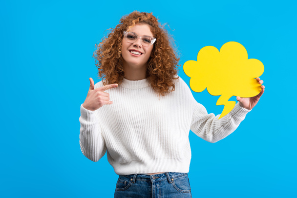 happy woman pointing at empty speech bubble in shape of cloud, isolated on blue  - Fotoğraf, Görsel