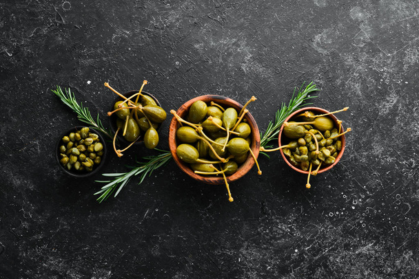 Capers. Marinated capers in a bowl on a black stone background. Top view. Free space for your text. - Foto, Bild