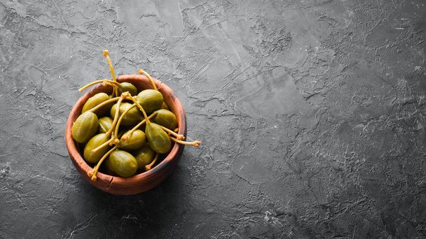 Capers. Marinated capers in a bowl on a black stone background. Top view. Free space for your text. - 写真・画像