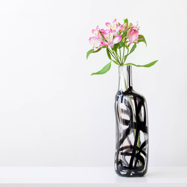 白いテーブルの上のガラス花瓶のピンクのarstroemeria - 写真・画像