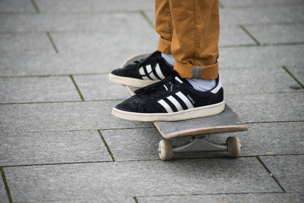 skater legs wearing black sneakers by Adidas  standing on skate board in the street - Foto, afbeelding