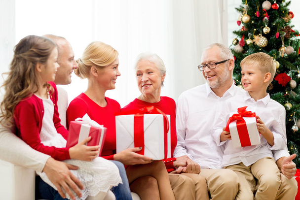 family, holidays, generation, christmas and people concept - smiling family with gift boxes sitting on couch at home - Fotó, kép