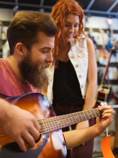 music, sale, people, musical instruments and entertainment concept - happy couple of musicians with guitar at music store - Foto, Imagem