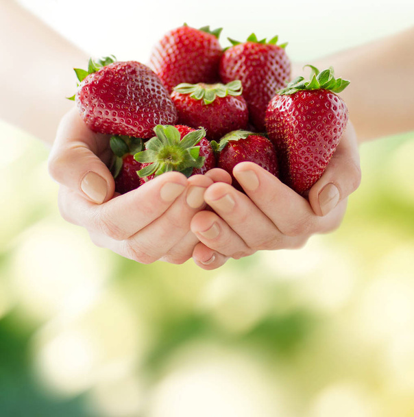summer, healthy eating, dieting, vegetarian food and people concept - close up of woman hands holding strawberries at home - Fotografie, Obrázek