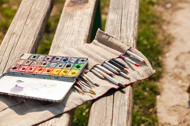 Art palette, watercolors, brushes on a wooden bench outdoors - 写真・画像