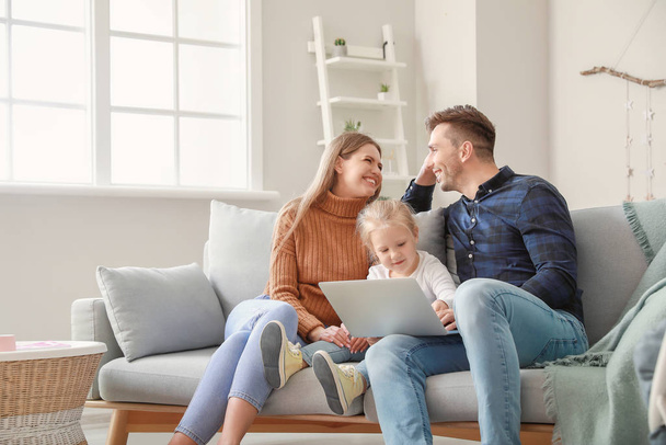 Onnellinen nuori perhe sylimikrolla istuu sohvalla kotona
 - Valokuva, kuva