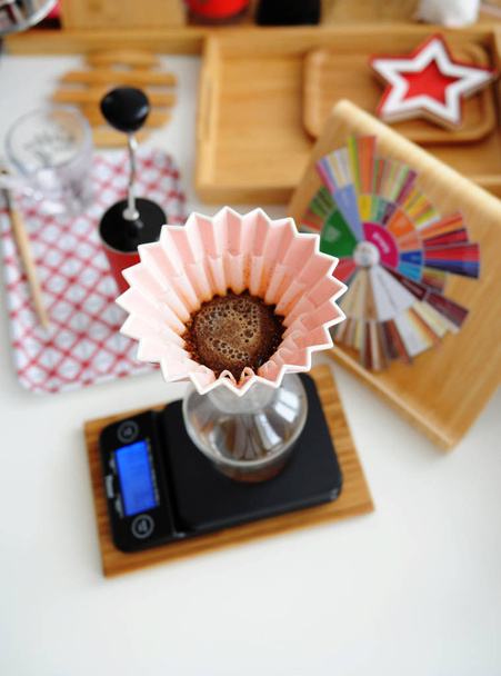 Alternatief handmatig brouwen. Giet water in koffie in roze keramische origami druppelaar met papier golf filter. Bovenaanzicht - Foto, afbeelding