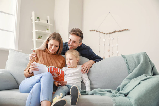 Χαρούμενη νεαρή οικογένεια ανάγνωση περιοδικό μόδας, ενώ κάθεται στον καναπέ στο σπίτι - Φωτογραφία, εικόνα