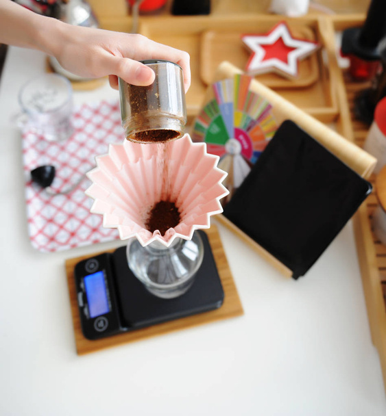 Alternatywne warzenie martwej natury. Wylewanie świeżo zmielonej kawy w różowym ceramicznym origami dripper z filtrem fali papieru. - Zdjęcie, obraz