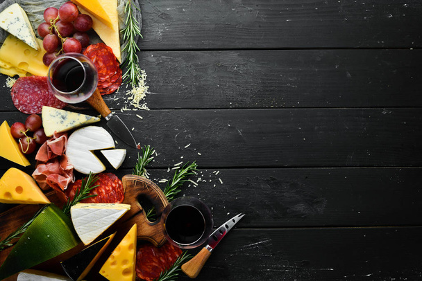 Italian appetizers. Cheese, wine, salami and prosciutto on a black stone background. Top view. Free space for your text. - Foto, Imagen