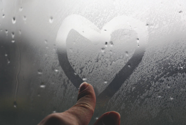 Szív az ablakon. Egy ujjal festették a ködös üvegre esőben. Fényes bokeh egy utcai lámpából. - Fotó, kép