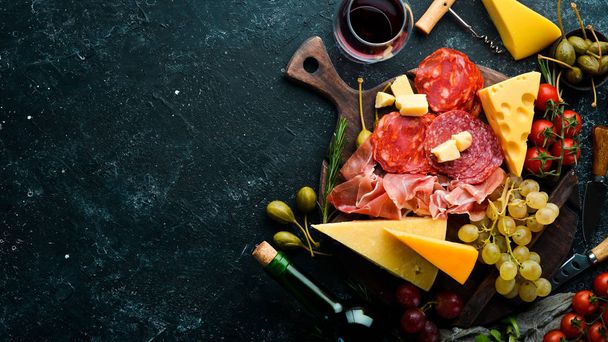 Italian appetizers. Cheese, wine, salami and prosciutto on a black stone background. Top view. Free space for your text. - Photo, Image