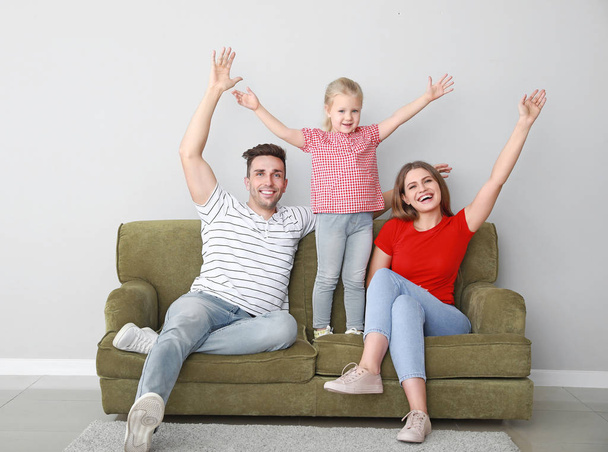Szczęśliwa młoda rodzina siedzi na kanapie w pobliżu światła ściany - Zdjęcie, obraz