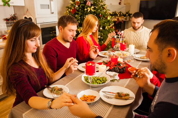 Νεαρή οικογένεια και φίλοι προσεύχονται και ευλογούν το τραπέζι στο Χριστουγεννιάτικο δείπνο - Φωτογραφία, εικόνα