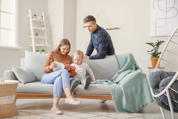 glückliche junge Familie liest Modezeitschrift, während sie zu Hause auf dem Sofa sitzt - Foto, Bild