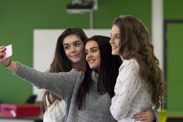 Three female students taking a selfie together on a smartphone in a classroom. - Fotografie, Obrázek