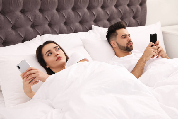 Young couple with smartphones in bed at home - Foto, imagen